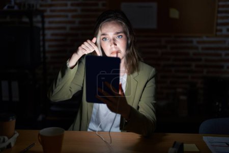 Photo for Blonde caucasian woman working at the office at night pointing down looking sad and upset, indicating direction with fingers, unhappy and depressed. - Royalty Free Image