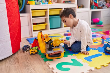Photo for Adorable hispanic boy playing with car toy sitting on floor at kindergarten - Royalty Free Image