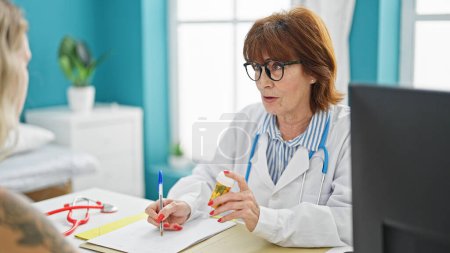 Téléchargez les photos : Femme d'âge moyen médecin et patient prescrivant des pilules en écrivant sur le document à la clinique - en image libre de droit