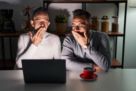 Photo for Homosexual couple using computer laptop bored yawning tired covering mouth with hand. restless and sleepiness. - Royalty Free Image