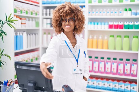 Foto de Farmacéutica mujer afroamericana sonriendo con confianza estrechan la mano en la farmacia - Imagen libre de derechos