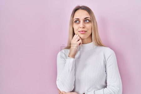 Photo for Young blonde woman wearing white sweater over pink background with hand on chin thinking about question, pensive expression. smiling with thoughtful face. doubt concept. - Royalty Free Image