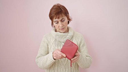 Photo for Mature hispanic woman looking at empty wallet over isolated pink background - Royalty Free Image