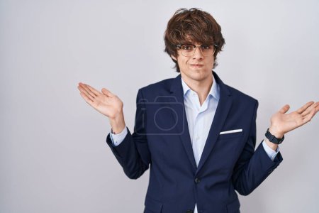 Photo for Hispanic business young man wearing glasses clueless and confused expression with arms and hands raised. doubt concept. - Royalty Free Image