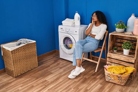 Foto de Joven latina aburrida esperando la lavadora en la sala de lavandería - Imagen libre de derechos