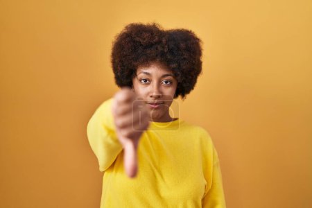 Photo for Young african american woman standing over yellow background looking unhappy and angry showing rejection and negative with thumbs down gesture. bad expression. - Royalty Free Image