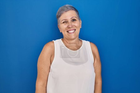 Photo for Middle age caucasian woman standing over blue background winking looking at the camera with sexy expression, cheerful and happy face. - Royalty Free Image