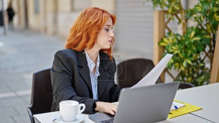 Téléchargez les photos : Jeune rousse femme d'affaires buvant du café document de lecture à la terrasse du café - en image libre de droit