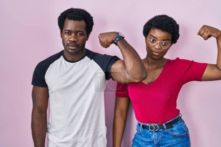 Foto de Joven africano americano pareja de pie sobre rosa fondo fuerte persona mostrando brazo músculo, confiado y orgulloso de poder - Imagen libre de derechos