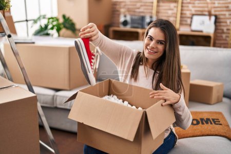 Photo for Young beautiful hispanic woman smiling confident unpacking sneakers of cardboard box at new home - Royalty Free Image