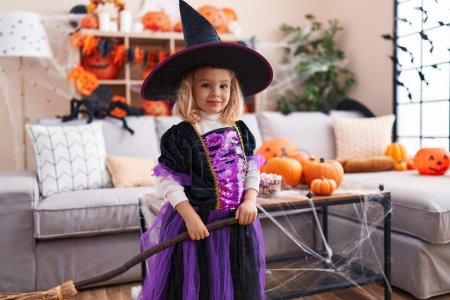 Foto de Adorable chica rubia con disfraz de bruja sosteniendo escoba en casa - Imagen libre de derechos