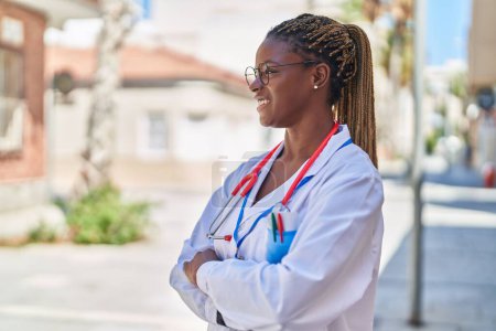 Téléchargez les photos : Femme afro-américaine médecin souriant confiant debout avec les bras croisés geste à la rue - en image libre de droit