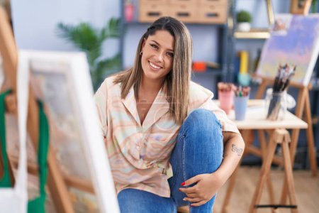 Photo for Young hispanic woman artist smiling confident sitting on floor at art studio - Royalty Free Image