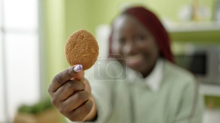Photo for African woman with braided hair holding cookie sitting on table at dinning room - Royalty Free Image
