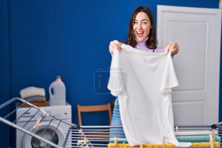 Junge brünette Frau, die Kleider an der Wäscheleine aufhängt, lächelt und lacht laut, weil lustig verrückter Witz. 