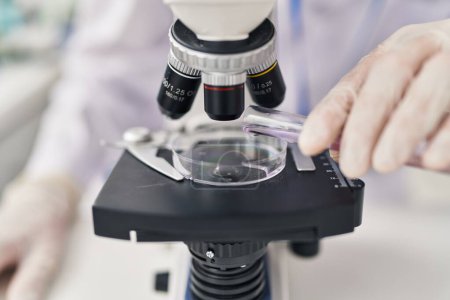 Téléchargez les photos : Jeune homme scientifique caucasien utilisant le microscope versant du liquide sur l'échantillon au laboratoire - en image libre de droit