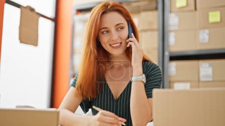 Téléchargez les photos : Jeune rousse femme ecommerce travailleur d'affaires parler sur smartphone écriture sur ordinateur portable au bureau - en image libre de droit