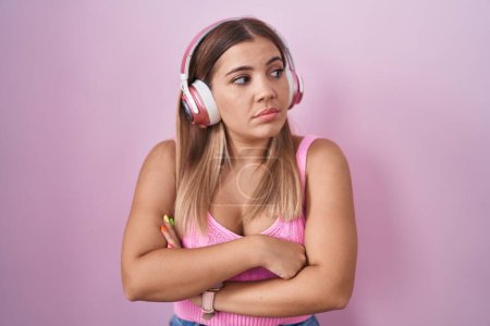 Téléchargez les photos : Jeune femme blonde écoutant de la musique à l'aide d'écouteurs regardant sur le côté avec les bras croisés convaincus et confiants - en image libre de droit