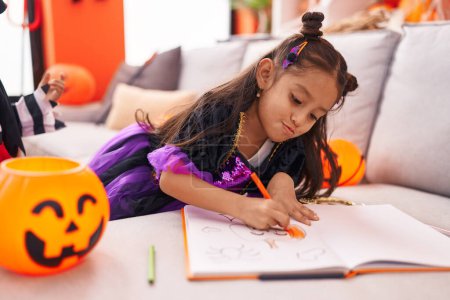 Foto de Adorable chica hispana dibujando en cuaderno teniendo fiesta de Halloween en casa - Imagen libre de derechos