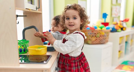 Photo for Adorable girls playing with play kitchen standing at kindergarten - Royalty Free Image