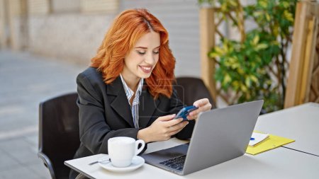 Téléchargez les photos : Jeune rousse femme d'affaires utilisant un smartphone sur la terrasse du café - en image libre de droit