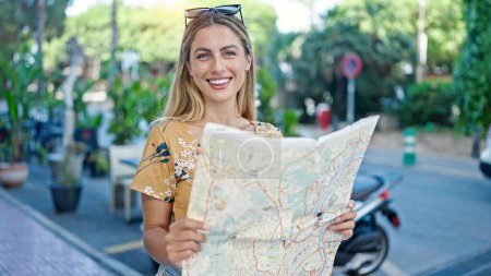 Foto de Joven mujer rubia turista sonriendo seguro buscando mapa de la ciudad en la calle - Imagen libre de derechos