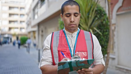 Photo for Young hispanic man volunteer holding clipboard at street - Royalty Free Image