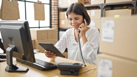 Photo for Young beautiful hispanic woman ecommerce business worker talking on telephone using touchpad at office - Royalty Free Image