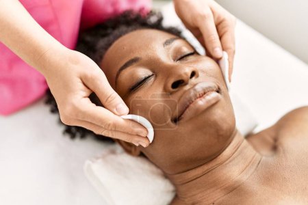 Téléchargez les photos : Femme afro-américaine allongée sur une table de massage ayant un traitement du visage au salon de beauté - en image libre de droit