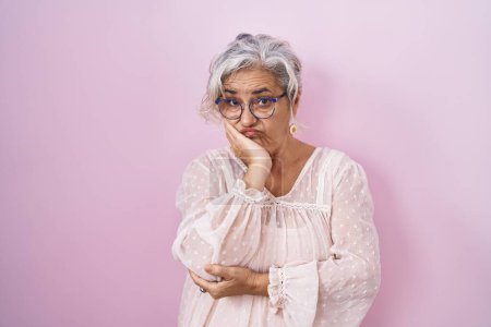 Téléchargez les photos : Femme d'âge moyen avec les cheveux gris debout sur fond rose pensant à la recherche fatigué et ennuyé avec des problèmes de dépression avec les bras croisés. - en image libre de droit