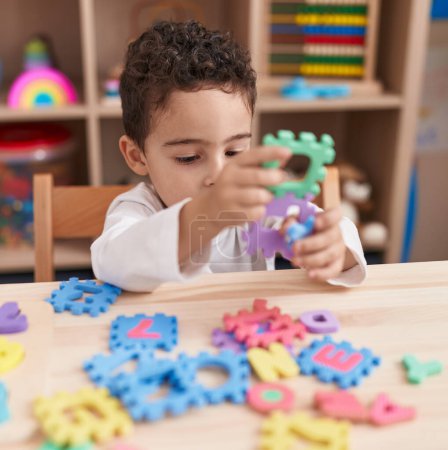 Foto de Adorable niño hispano jugando con el juego de puzzle de vocabulario sentado en la mesa en el jardín de infantes - Imagen libre de derechos