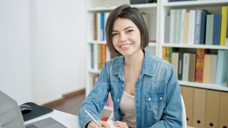 Photo for Young caucasian woman student using laptop writing on notebook at university classroom - Royalty Free Image