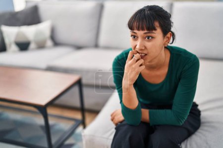 Photo for Young beautiful hispanic woman sitting on sofa with anxiety expression at home - Royalty Free Image