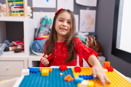 Photo for Adorable hispanic girl playing with construction blocks sitting on table at kindergarten - Royalty Free Image
