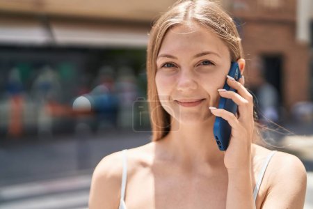 Téléchargez les photos : Jeune femme caucasienne souriant confiant parler sur le smartphone à la rue - en image libre de droit