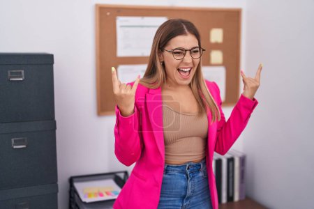 Photo for Young blonde woman standing at the office shouting with crazy expression doing rock symbol with hands up. music star. heavy concept. - Royalty Free Image