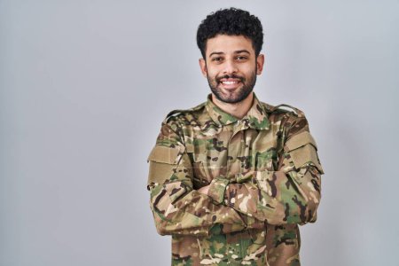 Foto de Hombre árabe vistiendo camuflaje uniforme del ejército cara feliz sonriendo con los brazos cruzados mirando a la cámara. persona positiva. - Imagen libre de derechos