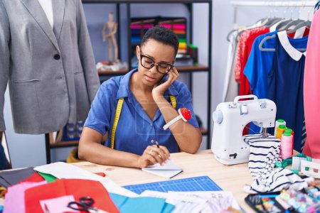 Téléchargez les photos : Femme afro-américaine tailleur parler sur smartphone écriture sur ordinateur portable au magasin de tailleur - en image libre de droit