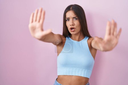 Photo for Young brunette woman standing over pink background doing stop gesture with hands palms, angry and frustration expression - Royalty Free Image