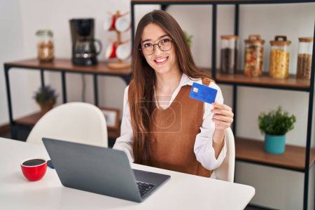 Photo for Young beautiful hispanic woman using laptop and credit card sitting on table at home - Royalty Free Image