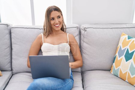 Téléchargez les photos : Jeune belle femme hispanique en utilisant un ordinateur portable assis sur la table à la maison - en image libre de droit