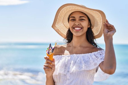 Foto de Joven africana americana turista sonriendo confiado comiendo helado en la playa - Imagen libre de derechos