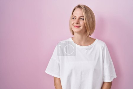 Foto de Young caucasian woman standing over pink background smiling looking to the side and staring away thinking. - Imagen libre de derechos