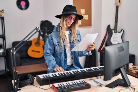 Foto de Young woman musician smiling confident playing piano keyboard at music studio - Imagen libre de derechos