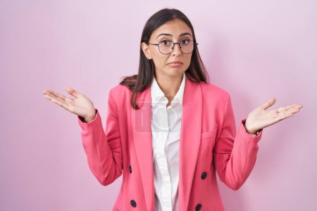 Photo for Young hispanic woman wearing business clothes and glasses clueless and confused expression with arms and hands raised. doubt concept. - Royalty Free Image