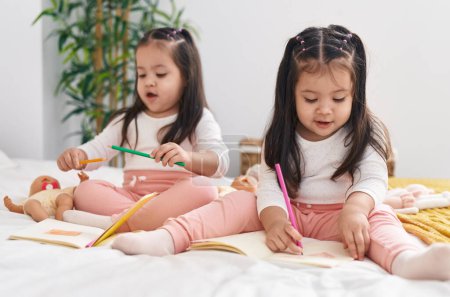 Foto de Adorables chicas gemelas dibujando en el cuaderno sentado en la cama en el dormitorio - Imagen libre de derechos