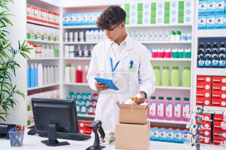 Photo for Young hispanic teenager pharmacist using touchpad holding pills at pharmacy - Royalty Free Image