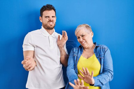 Photo for Young brazilian mother and son standing over blue background disgusted expression, displeased and fearful doing disgust face because aversion reaction. - Royalty Free Image