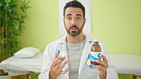 Téléchargez les photos : Jeune homme hispanique médecin tenant bouteille de médicaments parlant à la clinique - en image libre de droit