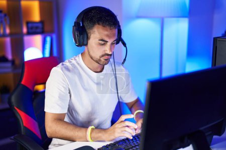 Téléchargez les photos : Jeune homme hispanique streamer jouer à un jeu vidéo en utilisant l'ordinateur à la salle de jeux - en image libre de droit